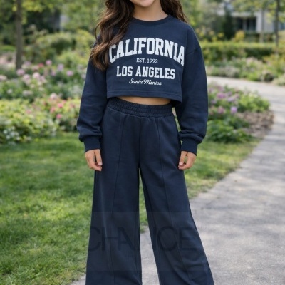 Menina com conjunto azul escuro com texto CALIFORNIA EST. 1992 LOS ANGELES Santa Monica e ténis brancos com riscas azuis ao ar livre