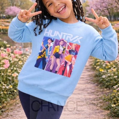 Camisola azul clara com estampado gráfico de personagens femininas e a palavra HUNTRXX.