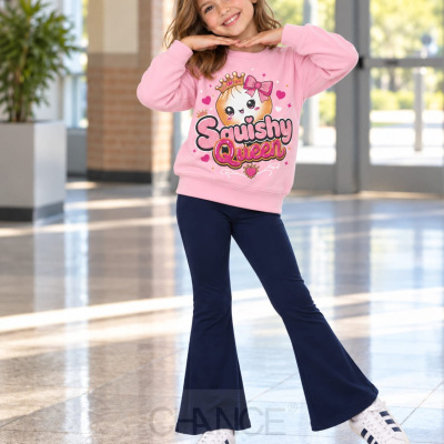 Menina com sweat rosa estampado Squishy Queen e calças azul-escuras num espaço interior iluminado