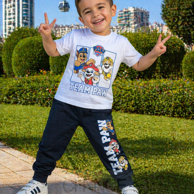 Menino sorridente com camisola branca e calças pretas PAW Patrol num jardim urbano