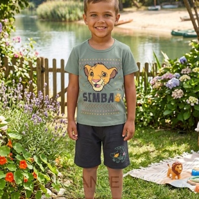 Conjunto infantil com t-shirt Simba, calções pretos e sapatilhas brancas num jardim junto a lago.
