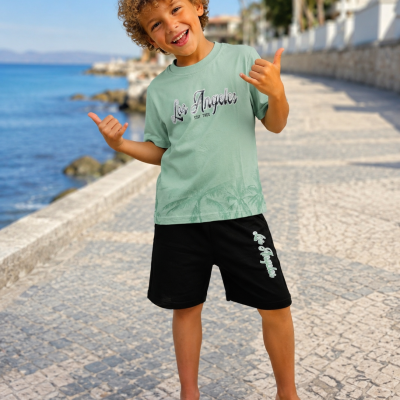 Rapaz com t-shirt verde clara e calções pretos em passeio à beira-mar em dia soalheiro