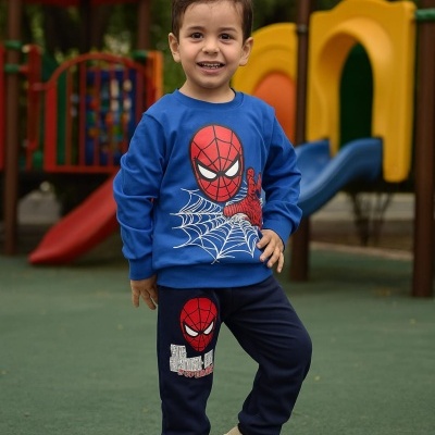Menino sorridente com fato de treino do Homem-Aranha junto a parque infantil colorido.