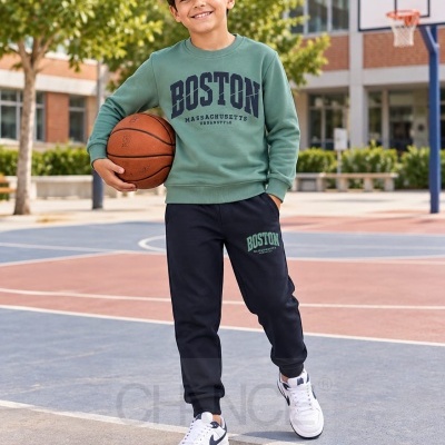 Menino com conjunto desportivo verde e preto segurando bola de basquetebol em campo exterior
