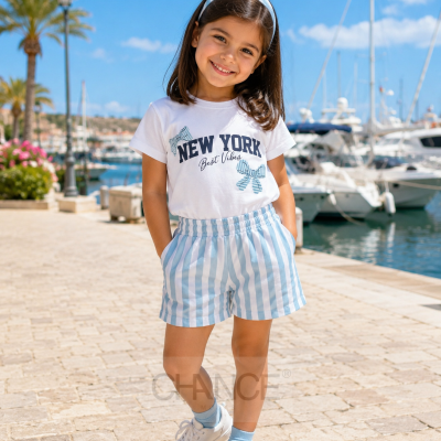Criança com roupa casual azul e branca num cais junto a barcos e palmeiras.