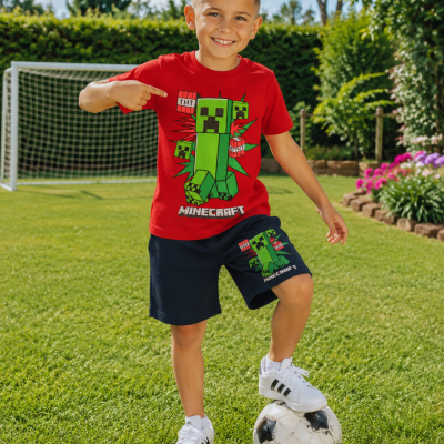 Camisola vermelha e calções azul escuro com estampado Minecraft numa criança a jogar futebol no relvado