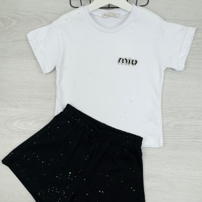 Conjunto infantil com t-shirt branca e saias pretas com manchas brancas em superfície clara