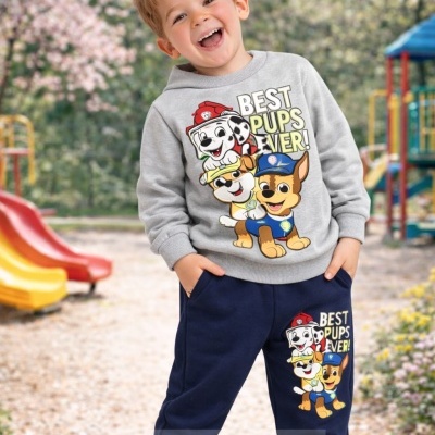 Menino com conjunto infantil cinzento e azul com estampado colorido de cães e texto, parque infantil ao fundo