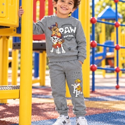 Menino em conjunto cinza PAW PATROL com personagens em parque infantil colorido.