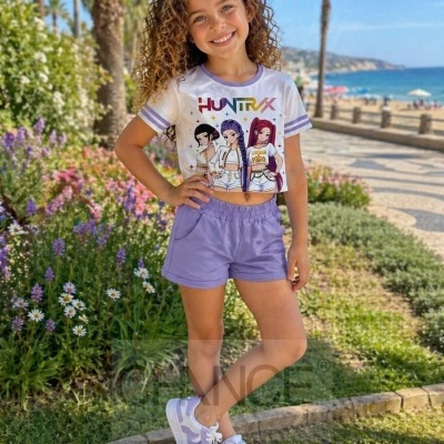 Menina sorridente com conjunto de roupa casual lilás e branca com t-shirt ilustrada ao ar livre perto da praia.