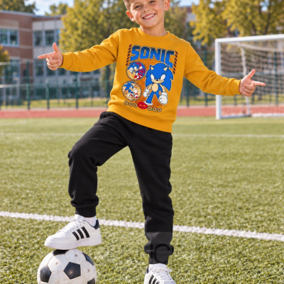 Menino com camisola amarela estampada do Sonic e calças pretas no campo de futebol.