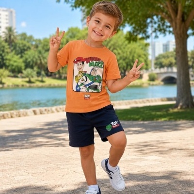 Criança em parque com t-shirt laranja com personagens Woody e Buzz, calções pretos e sapatilhas brancas.