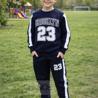 Menino com conjunto desportivo azul escuro com estampados brancos em parque.