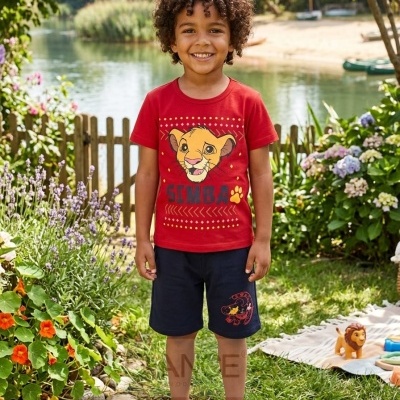 Criança veste camisola vermelha com Simba, calções azuis e ténis brancos ao ar livre junto a jardim e lago.