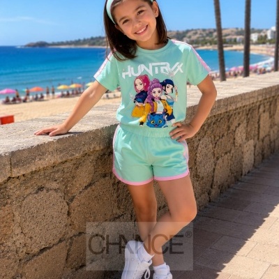Menina com conjunto verde-água e rosa com estampa HUNTRX junto à praia com mar e guarda-sóis coloridos