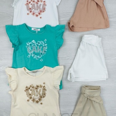 Conjunto infantil com t-shirts coloridas estampadas e calções em tons neutros sobre chão cinzento.