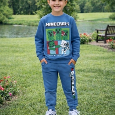 Menino com conjunto azul de algodão estampado Minecraft e ténis desportivos num jardim com lago e árvores