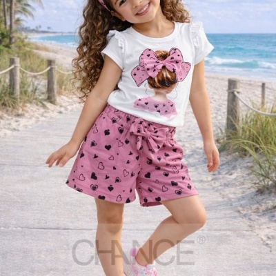 Conjunto infantil rosa e branco com corações e laço, modelo feliz numa praia