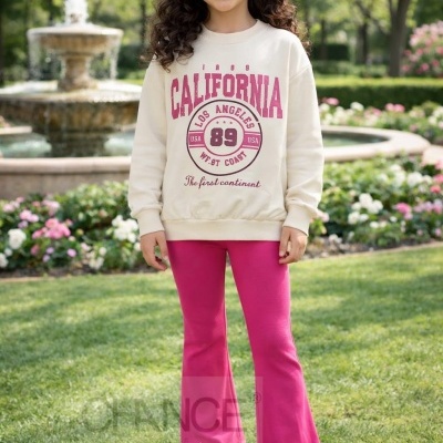 Menina com sweatshirt creme estampado rosa e borgonha, calças rosa e sapatilhas brancas num jardim com fonte ao fundo