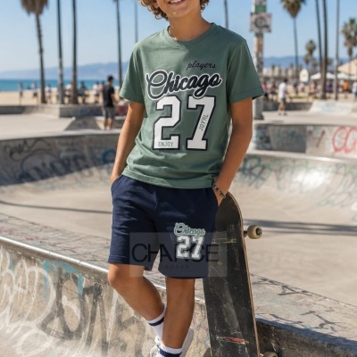 Menino com conjunto verde e azul, t-shirt e calções com texto Chicago 27, em skatepark com skate e palmeiras ao fundo.