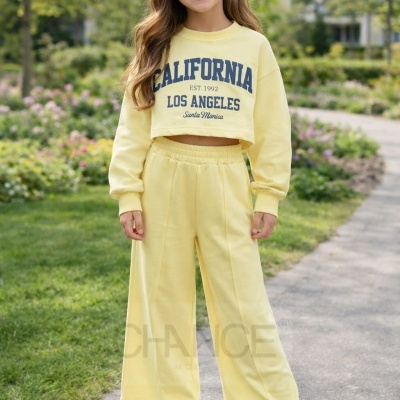 Criança com conjunto amarelo de sweatshirt cropped e calças largas, em ambiente de parque urbano.