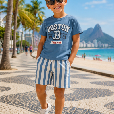 Menino com camisola azul BOSTON, calções às listas brancas e azuis, ténis brancos e óculos escuros na praia