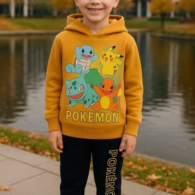 Menino com hoodie amarelo e calças pretas com tema Pokémon, ao ar livre junto a um lago