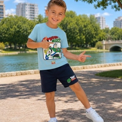 Menino com camiseta azul clara de Toy Story, calções azuis escuros e ténis brancos ao ar livre junto a um lago
