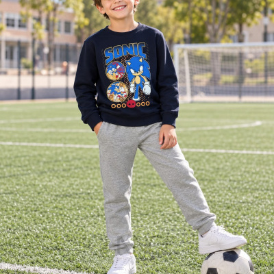 Criança com camisola azul do Sonic, calças cinza e ténis brancos num campo de futebol
