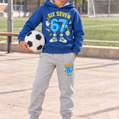 Menino com roupa desportiva azul e cinzenta segurando bola de futebol num campo exterior.