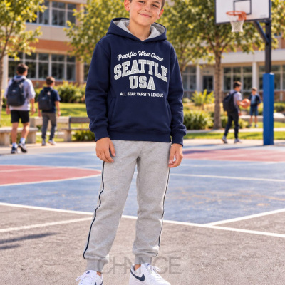 Rapaz com camisola azul escuro com texto branco, calças cinza e ténis brancos em campo de basquetebol ao ar livre