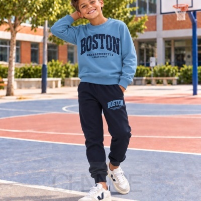 Criança com conjunto de roupa desportiva azul e azul escuro com texto BOSTON em campo de basquetebol
