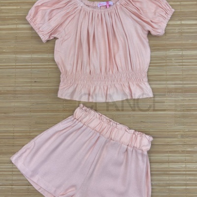 Conjunto de roupa de criança cor de rosa claro com blusa e calções numa tábua de madeira clara