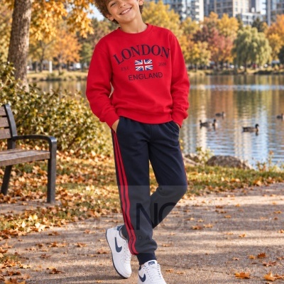 Rapaz com sweatshirt vermelho com texto LONDON EST 2026 ENGLAND e calças de treino azul com riscas vermelhas num parque no outono