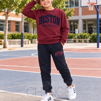 Menino a sorrir vestindo conjunto com sweatshirt e calças de treino, em campo de basquetebol.