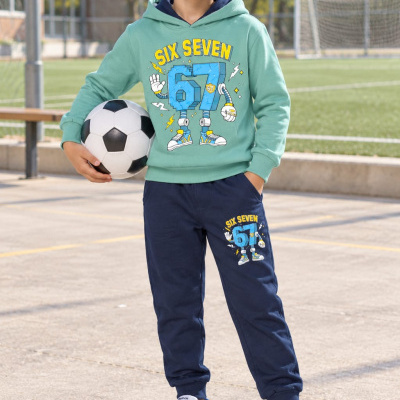 Menino com conjunto de roupa verde e azul escuro com estampado SIX SEVEN 67 a segurar uma bola de futebol num campo.
