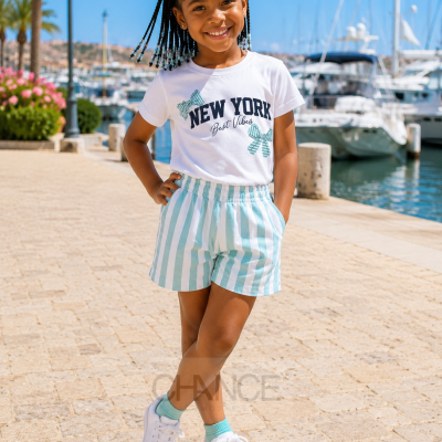 Menina a sorrir vestida com T-shirt branca e calções às riscas num cais com barcos ao fundo