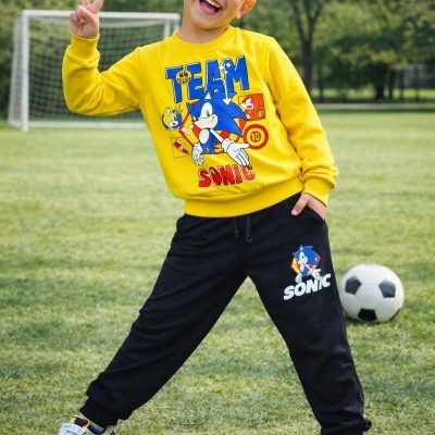 Menino com conjunto amarelo e preto com estampados do Sonic num campo de futebol
