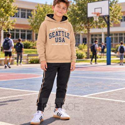 Criança com hoodie bege com texto Seattle USA e calças pretas num campo de basquetebol ao ar livre