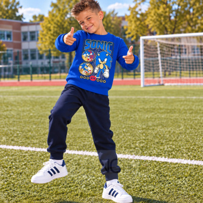 Menino a usar roupa azul com estampa Sonic em campo de futebol.