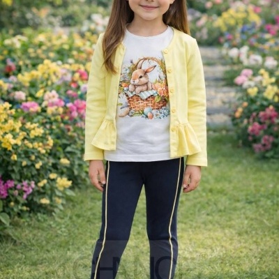 Menina com cardigan amarelo claro, t-shirt branca com estampa de coelho, leggings pretas com riscas amarelas e sapatilhas brancas, em jardim florido