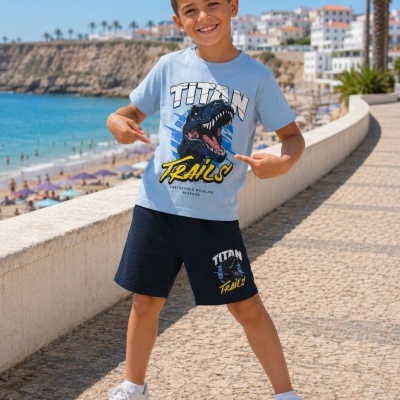 Menino com conjunto de roupa azul com dinossauro junto ao mar