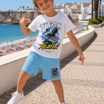 Criança a usar conjunto branco e azul com estampa de dinossauro, na praia, a apontar para a roupa