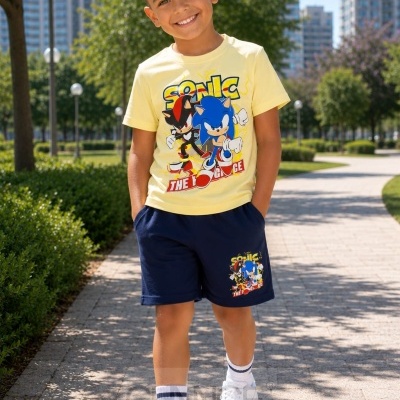 Menino com conjunto de roupa infantil Sonic, t-shirt amarela e calções azul escuro, em passeio urbano com árvores e prédios ao fundo.