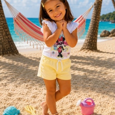 Criança sorridente com roupa amarela e branca na praia com brinquedos de areia coloridos