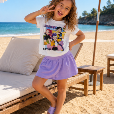 Menina de t-shirt branca com estampa K-POP e saia lilás na praia ao lado de cadeiras de madeira e guarda-sóis