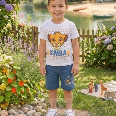 Rapaz com camisola branca estampada com Simba, calções azuis e ténis brancos na relva perto de flores e brinquedos de madeira