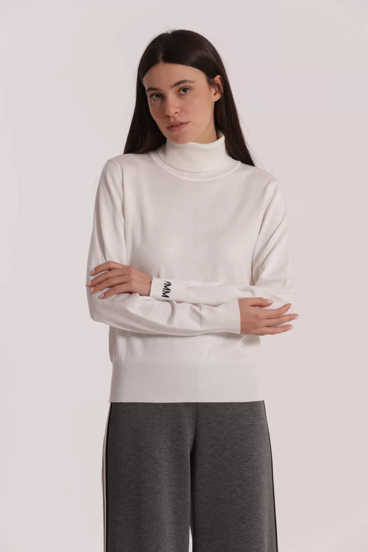 Mulher com camisola branca de gola alta e calças cinzentas com risca lateral