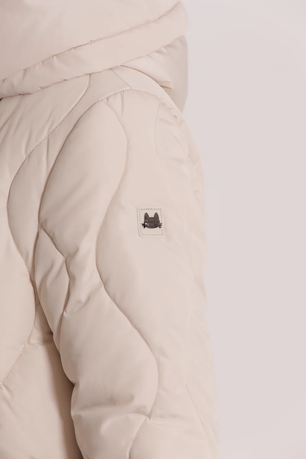Casaco acolchoado bege claro com emblema preto de gato na manga