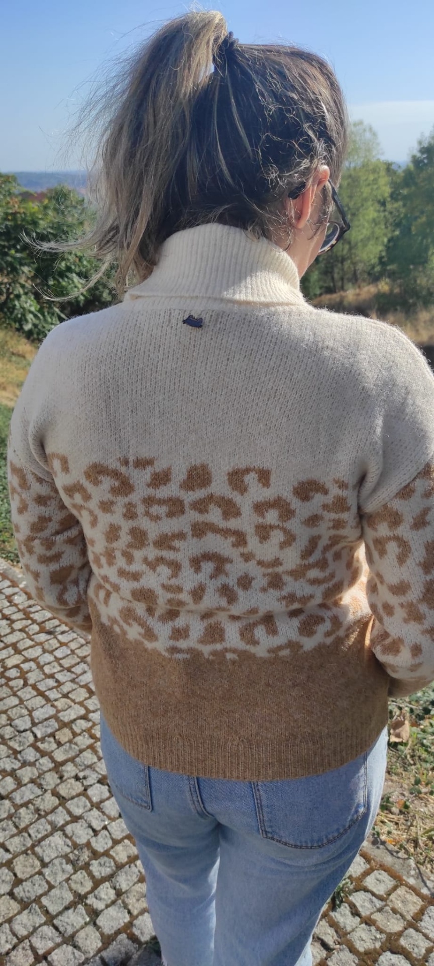 Pessoa de costas a usar camisola creme com padrão animal castanho e jeans azuis ao ar livre